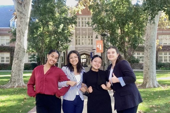 Four students wearing professional attire are standing together in front of Knoles Hall.