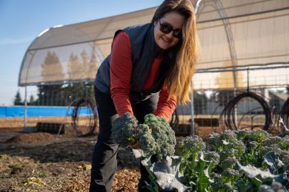 Jessica Coleman holds broccoli while working in a garden